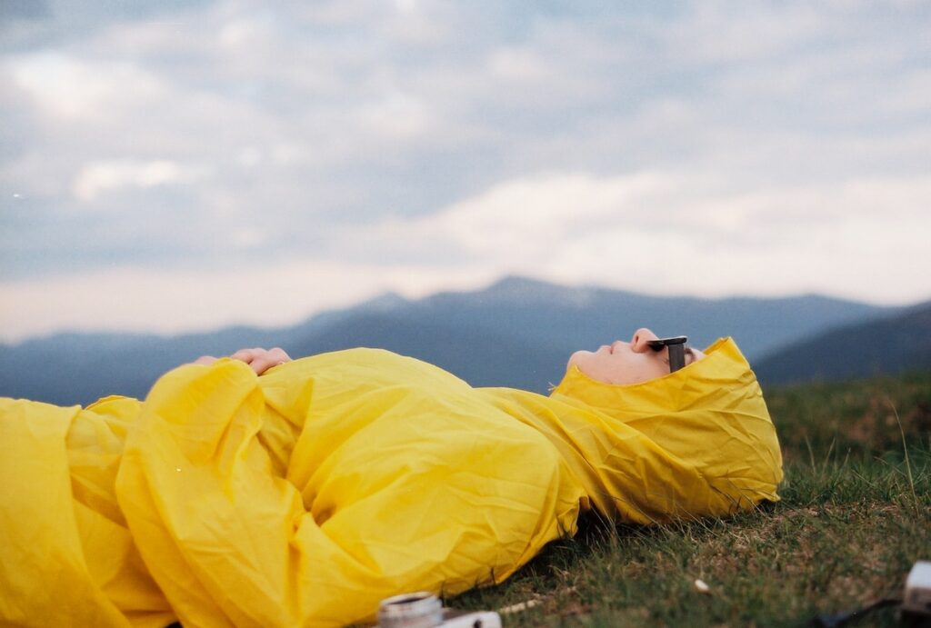 man in yellow hoodie lying on green grass field under white cloudy sky during daytime