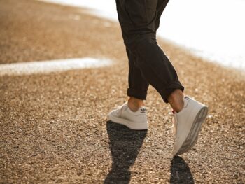 person in black pants and white sneakers walking on brown asphalt road during daytime