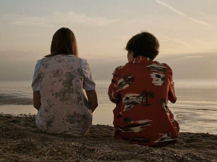 2 women sitting on brown sand during daytime
